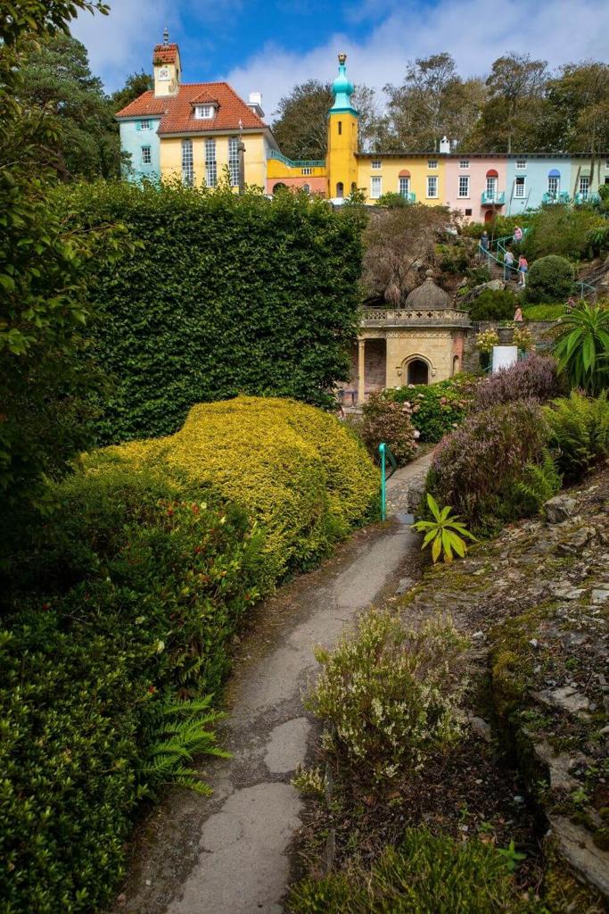 A picture of a garden with a path leading towards the colourful village of Portmeirion in Snowdonia